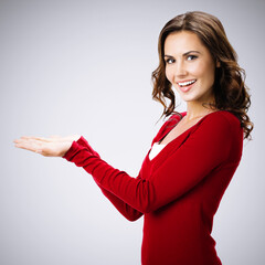 Beautiful young woman showing something, on grey