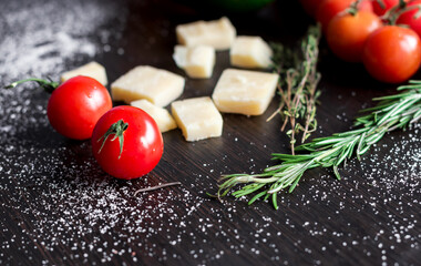 Cherry tomatoes, cheese, thyme and rosemary on the dark wooden table. Cooking at home. Simple ingredients. Concept of healthy eating habits.