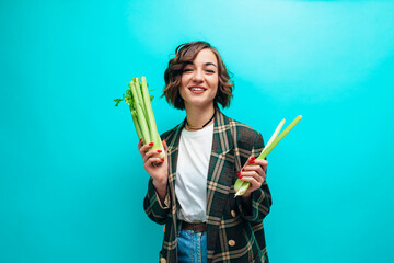 Happy woman holding fresh green celery wearing casual isolated over blue background. Healthy lifestyle concept - Powered by Adobe