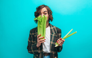 Happy woman holding fresh green celery wearing casual isolated over blue background. Healthy...