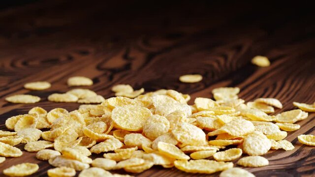Corn flakes falling onto wooden surface, traditional dry breakfast cereal close up