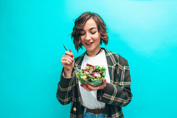 Happy healthy young woman eating natural salad wearing casual isolated over blue background. Healthy lifestyle concept