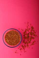 Glass jar with brown rice on a pink background.