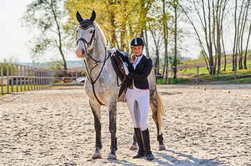 Beautiful horse rider girl stands near a white horse on a farm