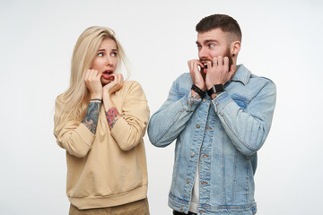 Studio photo of young frightened attractive couple holding raised hands on their faces and looking...