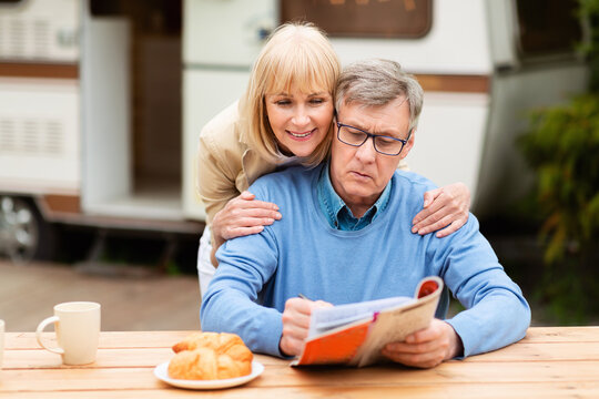 Mature Woman Helping Her Husband Solve Crossword Puzzle Near Trailer Outdoors