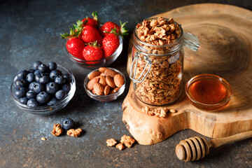 Homemade oatmeal granola in glass jar with berries on dark background.