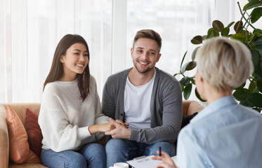 Smiling Multiethnic Spouses Holding Hands Reconciling Sitting In Psychotherapist's Office