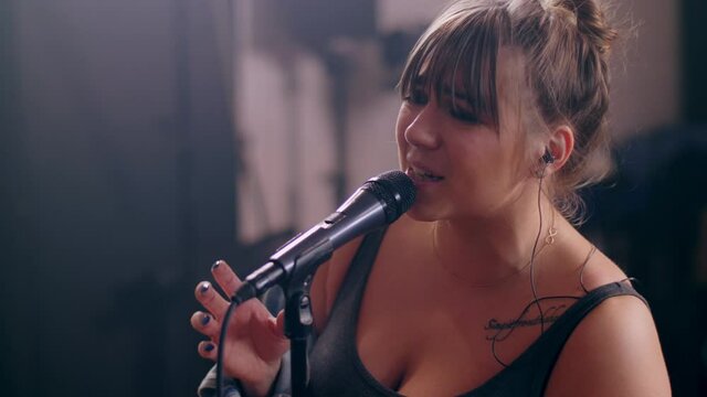 Tilt up talented young girl soloist singing on microphone and gesticulating on rock performance