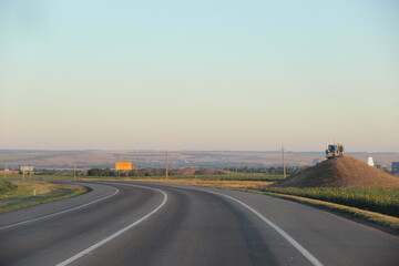 Morning turn of the road in the steppe against the background of a tractor