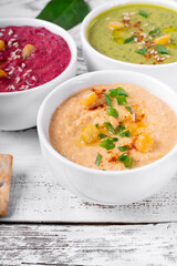 Colorful hummus in the white bowls on the white wooden table. Classic, beetroot and spinach chickpea dips