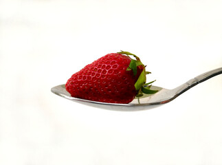 Close up of ripe strawberry with its leaves on a spoon with a white background. Delicious dessert for healthy eating. Strawberry is issued from organic farming
