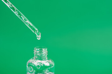 A drop of hemp oil from a pipette into a bottle. Bottle with hyaluronic acid on a green background