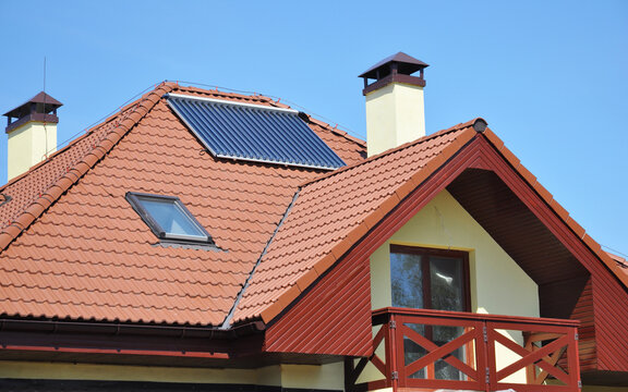 A modern house with metal tiled roof, skylight, solar panel, chimney, open balcony and window in the attic.