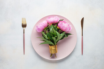 Pink peony flowers and a plate with cutlery on the table. Top view. Flat lay
