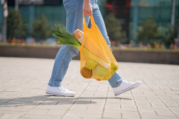 Woman in blue jeans holding eco-friendly string reusable net bag with fruits and vegetables. Ingredient in healthy, dietary and vegetarian food. 