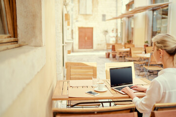 Technology and travel. Working outdoors. Freelance concept. Copy space on the screen. Close up of  young woman using laptop in sidewalk cafe on ancient europian street.