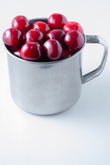 Sweet cherries in a steel mug on a white paper background