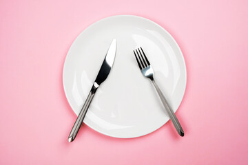 White plate on a pink background. The fork and knife are on the plate