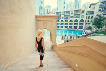 Beautiful young woman in black dress with hat walking on Dubai Downtown.