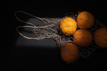 Fototapeta na wymiar String bag with oranges on black background. Organic eco bio products from farm. New harvest. Ingredient in healthy, dietary and vegetarian food. Top view
