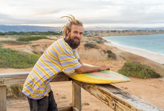 Portrait of Hipster Surfer with dreadlocks and beard looking at the ocean with vintage surfboard . - Powered by Adobe