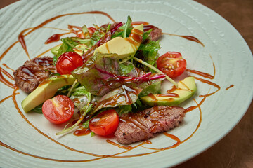 Salad with grilled beef, arugula, cherry tomatoes, avocado in a white ceramic plate on a copper, metal background. Close up. Warm meat salad