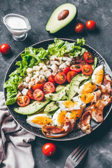 Cobb salad with chicken, avocado, tomatoes, eggs, bacon and cheese on a black  table.