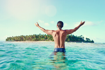 Vacation and freedom. Happy young man rising hands up bathing on tropical beach enjoying beautiful view.