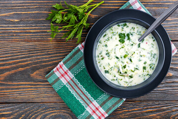 Cold soup with fresh cucumbers, radishes with yogurt in a bowl on wooden background. Traditional Russian food - okroshka. Vegetarian food. View from above. Healthy food concept.