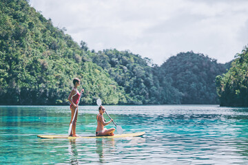 Summer holidays vacation travel. SUP Stand up paddle board. Young women sailing together on...
