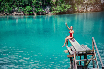 Vacation and activity. Young woman in swimsuit enjoying blue tropical lagoon view sitting on wooden springboard. Siargao Island, Philippines. © Loginova