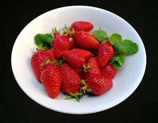 Fresh ripe strawberries, small green leaf and mint sprig  in white bowl on the dark grey background. Top view
