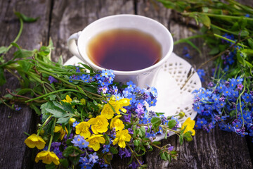 Herbal tea in a white vintage ceramic cup, fresh forget-me-not flowers on a wooden boards background