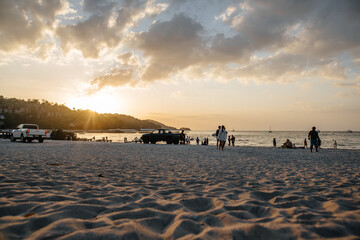 Thailand, 2020: coastline on sunset, people are greeting sunset on the beach, people and cars silhouettes