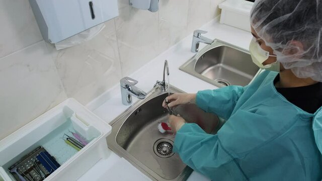 Wide shot of Woman technician in white gloves wash dental medical instruments under a stream of distilled water and puts them on a clean towel. Before the disinfection procedure of orthodontic pliers.