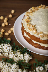 Carrot cake, branch with white flowers and hazel nuts on the wooden table