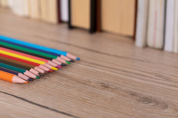 Obraz premium Colored pencil crayons are lying on the desk top next to a series of books.