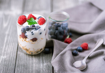 White yogurt in glass jar with blueberries on grey background.