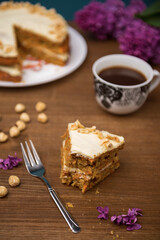 Piece of carrot cake with carrot cake and a cup of coffee with bouquet of lilac on the background