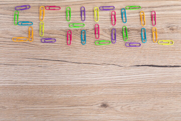 Colorful paper clips arranged in an inscription - school. Wooden top of the school desk.