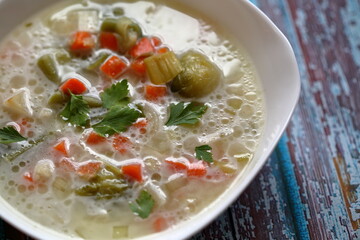 Traditional Polish vegetable soup in white plate, decorated with green parsley leaves, partly in soft focus, on old rustic blue painted wooden table close up