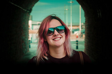 mujer con gafas de sol y pelo rosa posando en un túnel