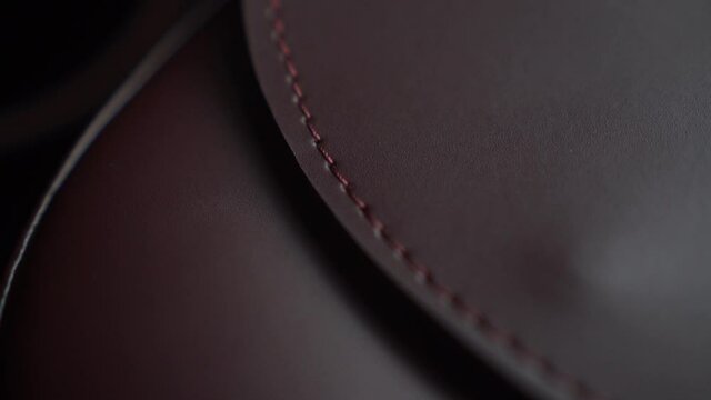 Close Up Woman Fashion Genuine Leather Texture Burgundy Bag Gold Metal Handcrafted Backstich Motion Shots Acsessories Clasp and Belt Details Concept Macro Stich on a Black Background 
