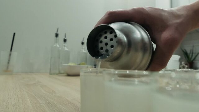 Cocktail poured from shaker into glasses by bartender. Close up, slow motion