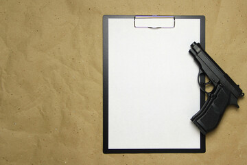 A tablet with a white sheet of A4 format with gun on a beige craft paper. Concept of the legal system, criminal organizations, security services. Stock photo with empty place for your text and design.