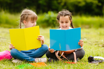two pretty schoolgirls sit with books outdoors in the park. Schoolgirls or students are taught...