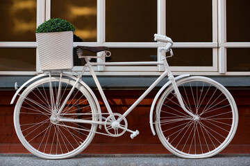 Old white vintage bicycle with a basket, leaning against a brick wall on the street.
