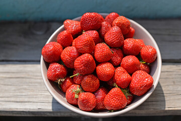 
ripe juicy strawberry berry in a plate on a wooden background under the sun
