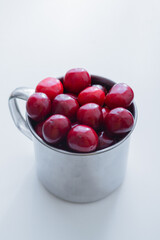 Sweet cherries in a steel mug on a white paper background